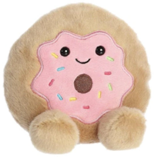 A plush toy resembling a donut with a pink top, multicolored sprinkles, and a smiling face, with beige fur and a round shape.