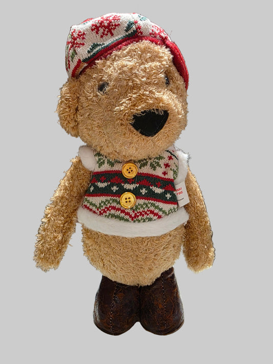 Teddy bear wearing a festive sweater and hat on a gray background