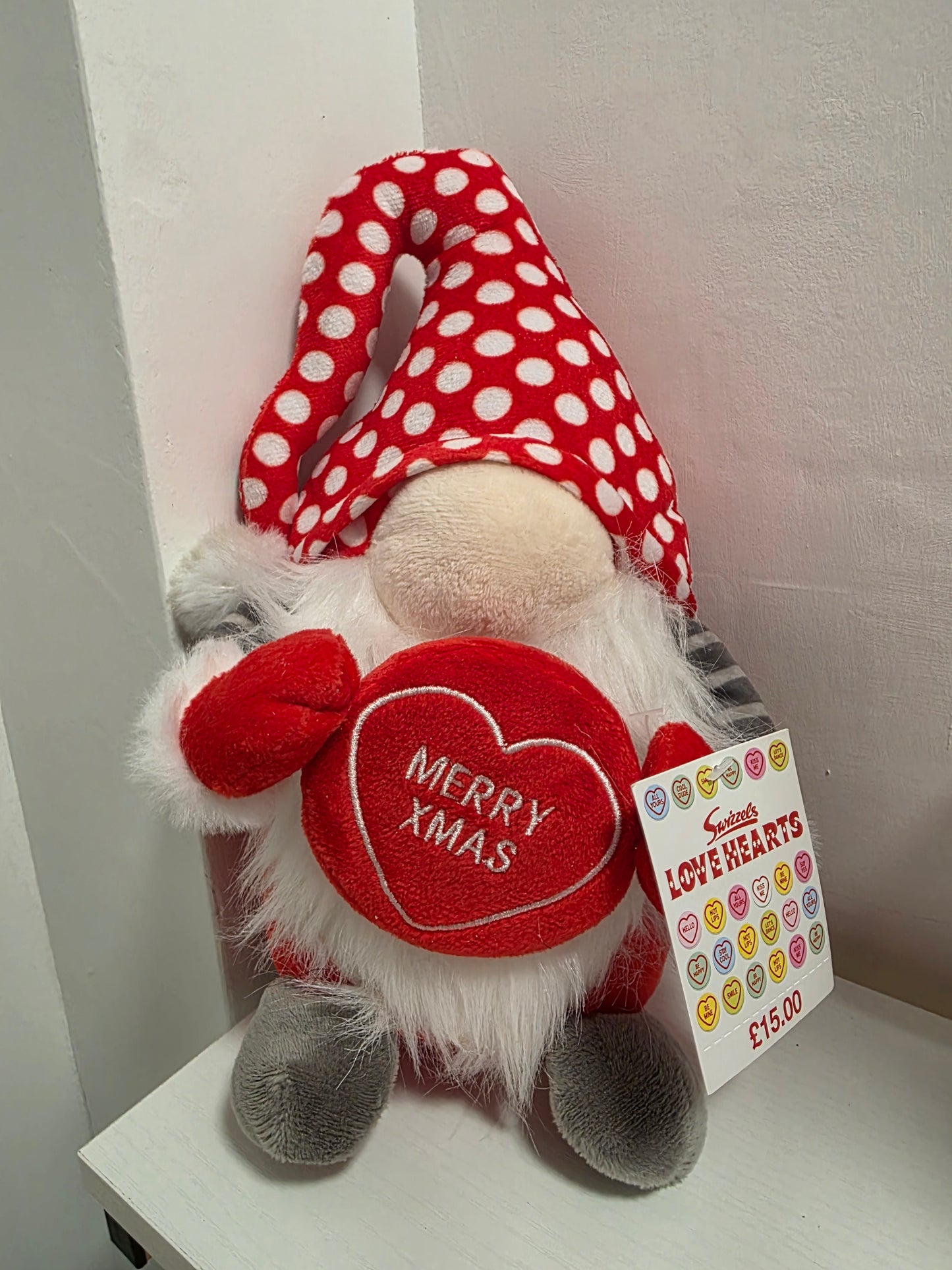 Plush gnome toy with red and white polka dot hat and 'Merry Xmas' heart, on a light background.