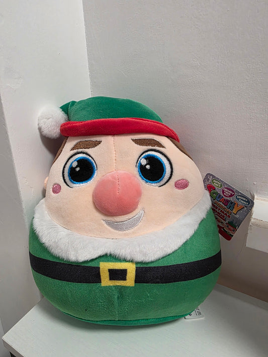Plush toy resembling a character with a green outfit and red hat on a white surface.