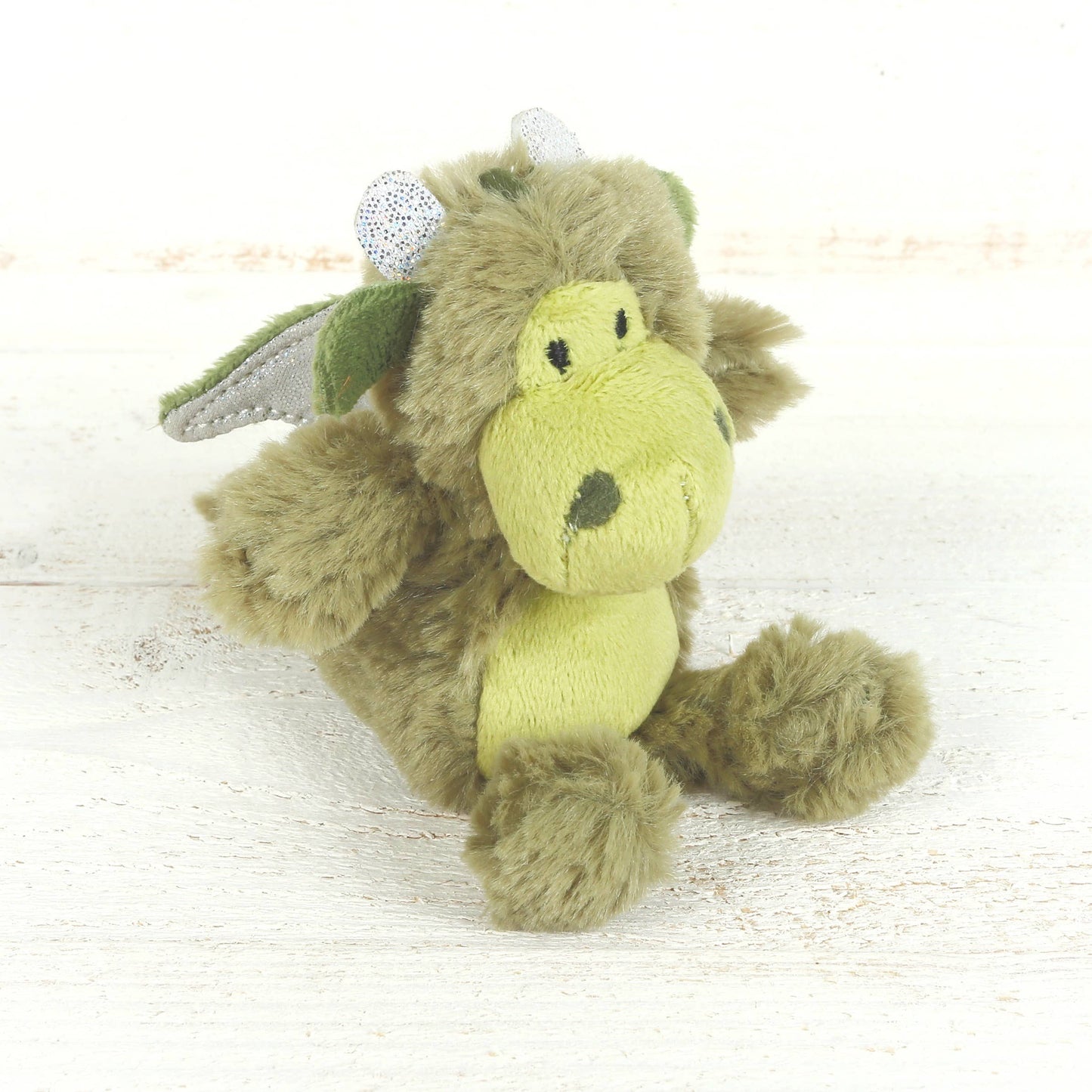 Green plush dragon toy on a light wooden surface