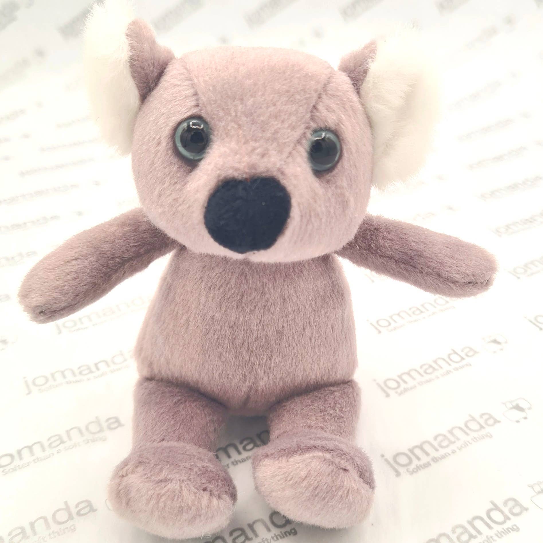 Plush koala toy with large eyes and a black nose on a white background with 'jomanda' branding.