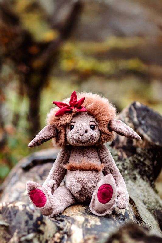 Stuffed animal with large ears and a red bow sitting on a rock in a natural setting
