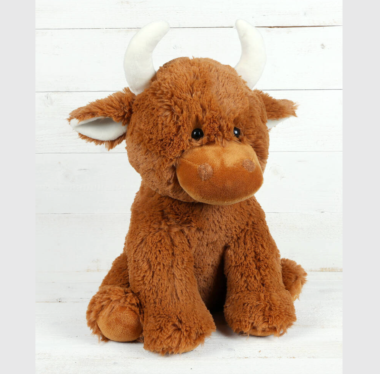 Plush toy Highland cow on a white wooden background