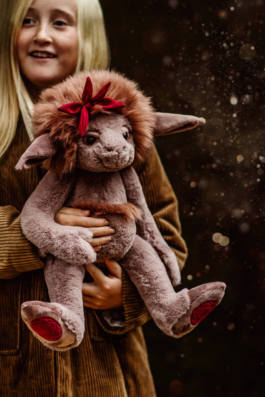 Child holding a plush toy with a red bow against a dark background