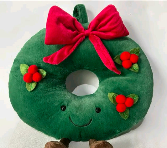 Plush toy shaped like a Christmas wreath with a red bow and holly leaves on a white background